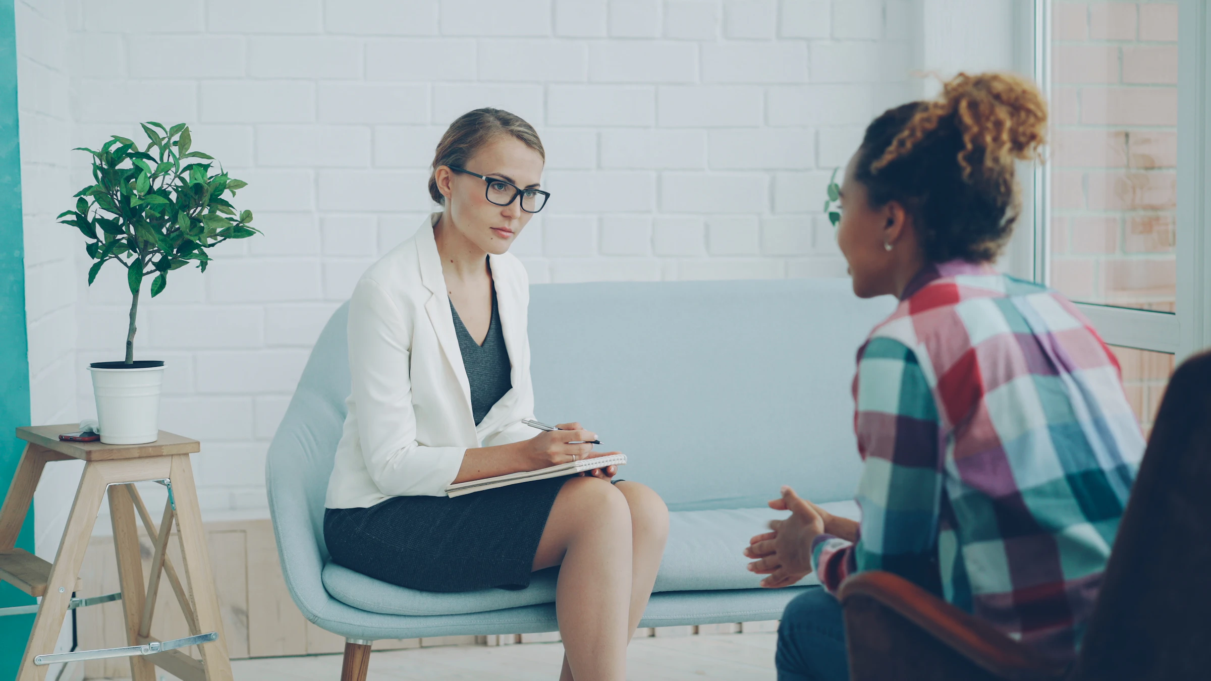 Psicóloga tomando notas mientras conversa con una paciente en un consultorio iluminado